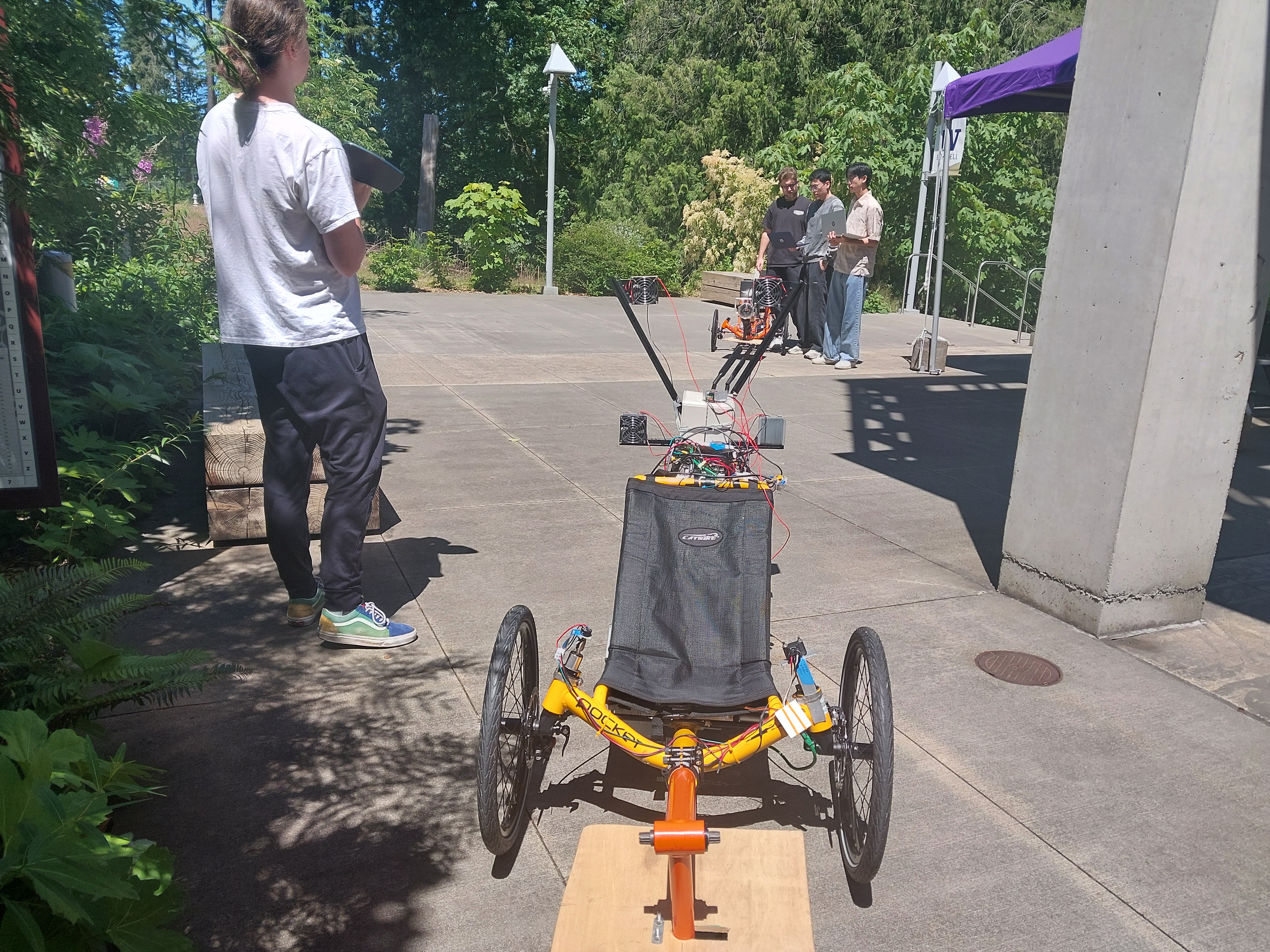 Students stand outside with a yellow and orange autonomous trikes to test the coupling system between the two.