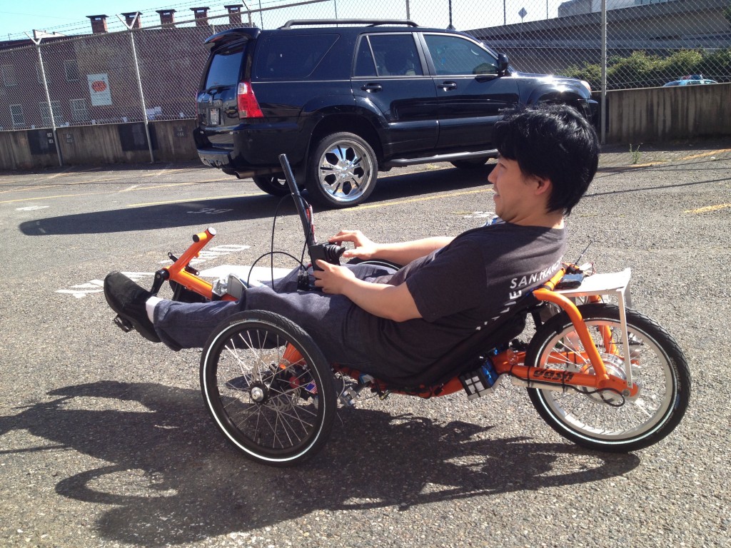 A person rides an orange autonomous trike in a parking lot.