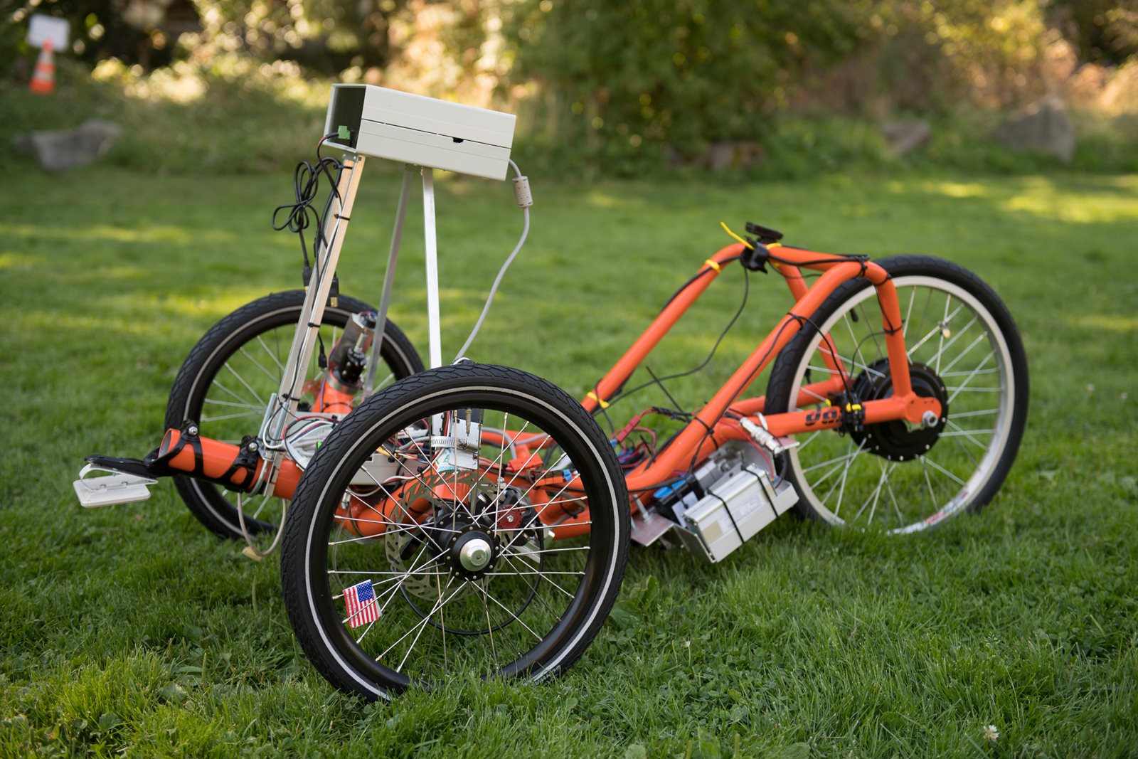 An orange autonomous trike in a grassy field.