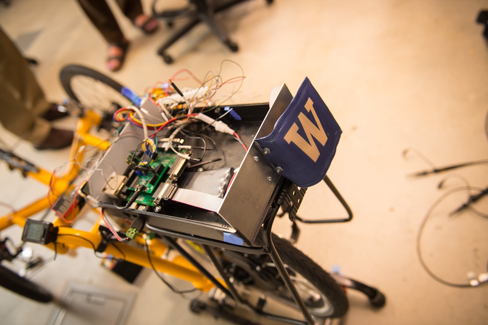 The electrical box of a yellow autonomous trike with a purple and gold University of Washington W.